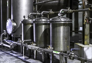 Piping and tanks inside an industrial setting with stainless steel fittings and pressure regulators