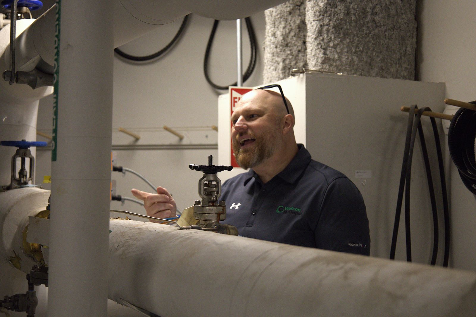 Rob Warnell explaining beside insulated piping and a valve in a mechanical room