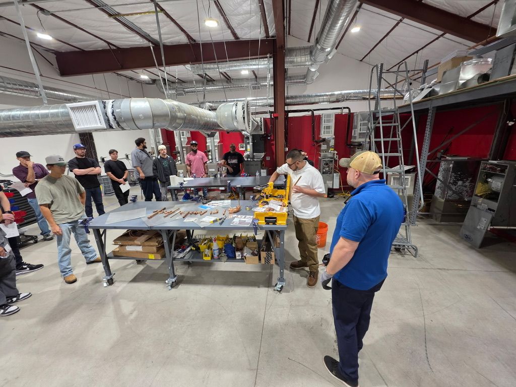Rob Warnell leading a hands-on press-fitting class while an instructor demonstrates copper press fittings to trainees